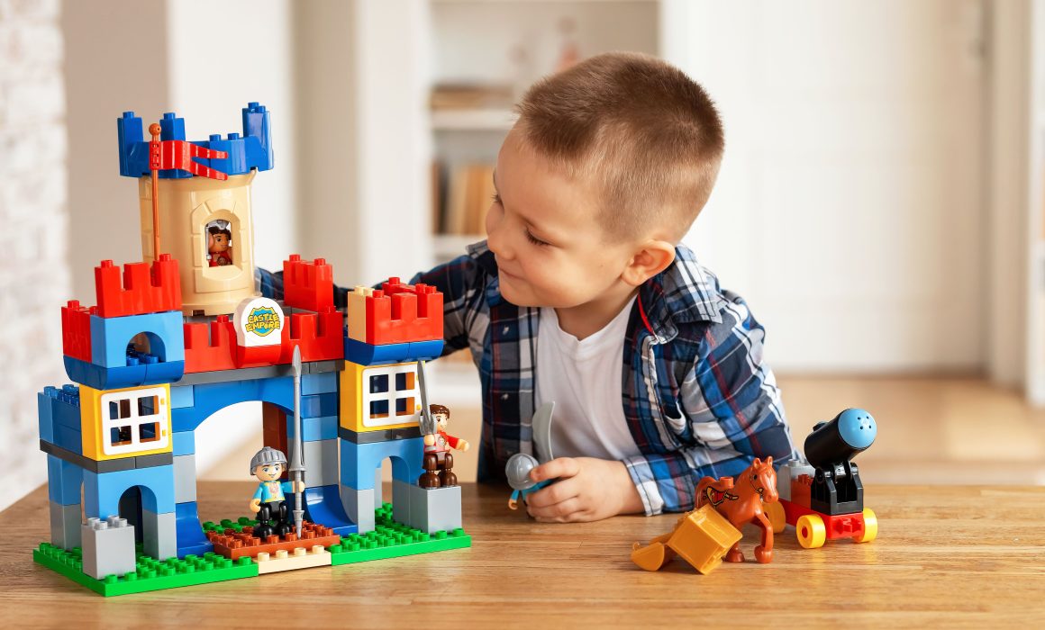 Young boy playing creatively with toy castle and figurines indoors, fostering imagination.