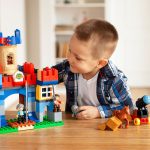 Young boy playing creatively with toy castle and figurines indoors, fostering imagination.