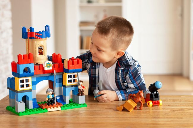 Young boy playing creatively with toy castle and figurines indoors, fostering imagination.