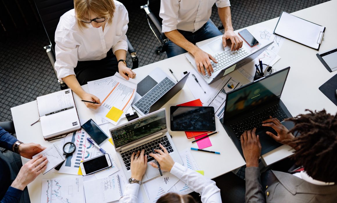 Vibrant office teamwork scene with laptops, documents, and diverse professionals in a meeting.